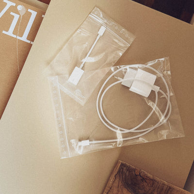 Two transparent plastic bags containing various small white electronic parts and cables, lying on a brown cardboard surface.